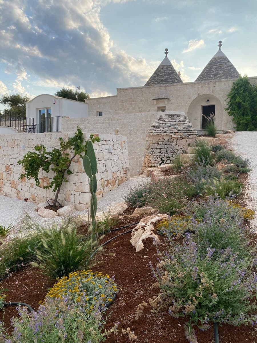 Il giardino appena piantato davanti ai trulli, con un piccolo trullo in pietra a secco e l’arco d’ingresso
