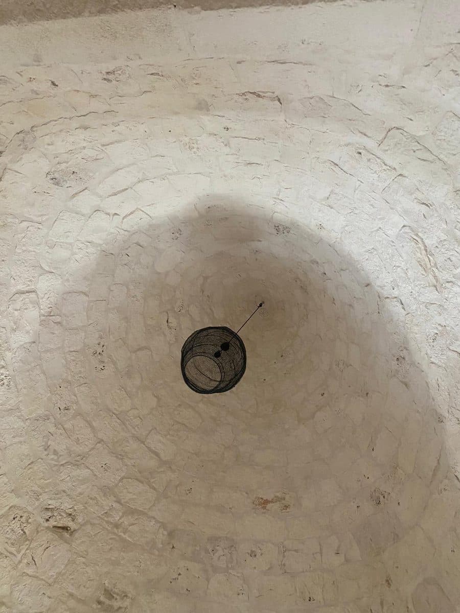 L’interno di un cono visto dal basso, con le pietre a vista disposte in cerchi e una lampada sospesa