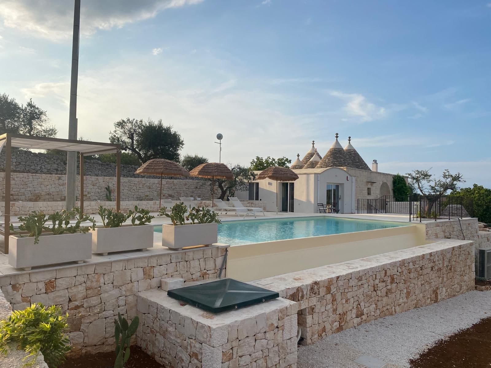 La piscina a sfioro con i lettini, gli ombrelloni di paglia e i trulli sullo sfondo